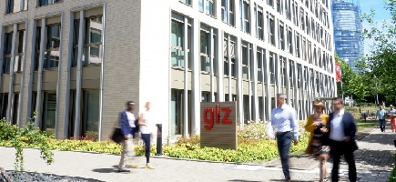 Menschen vor einem Bürogebäude, vor dem ein Schild mit der Aufschrift GIZ steht.