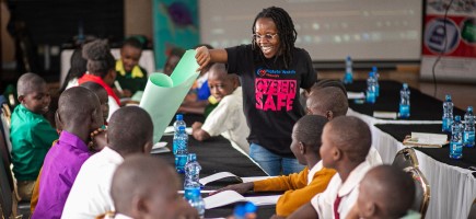A woman hands a poster to a group of young people. Her T-shirt bears the words ‘Cyber Safe’.