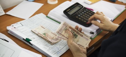 A person holds money in her hand and types on a calculator.