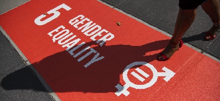 High-heeled shoes are walking across a floor. It shows the icon for Goal 5 of the Sustainable Development Goals.